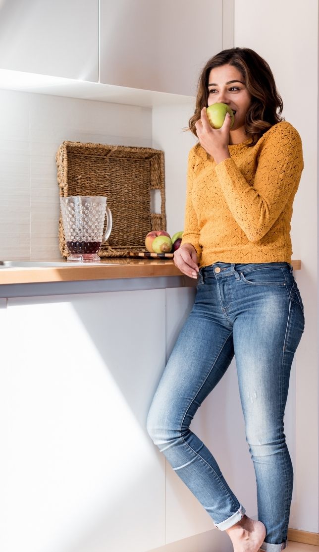 woman standing in kitchen eating green apple